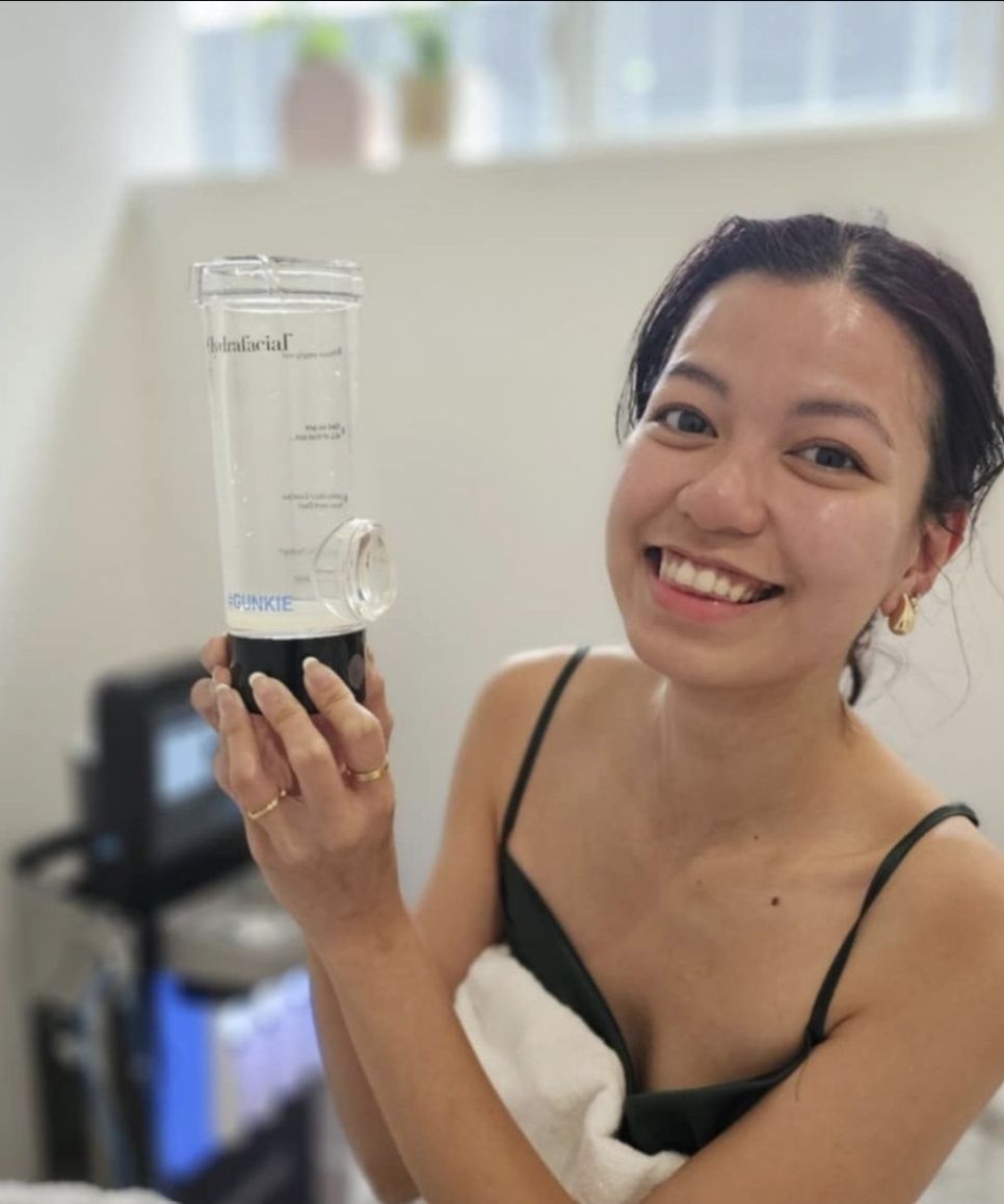 A smiling client holds up the Hydrofacial collection jar after her treatment